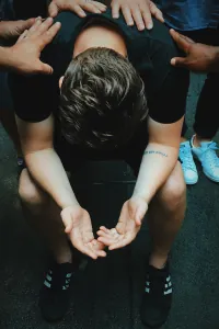 Person sitting with head bowed while others offer support
