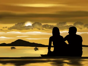 Silhouettes of a couple sitting together beside the water at sunset